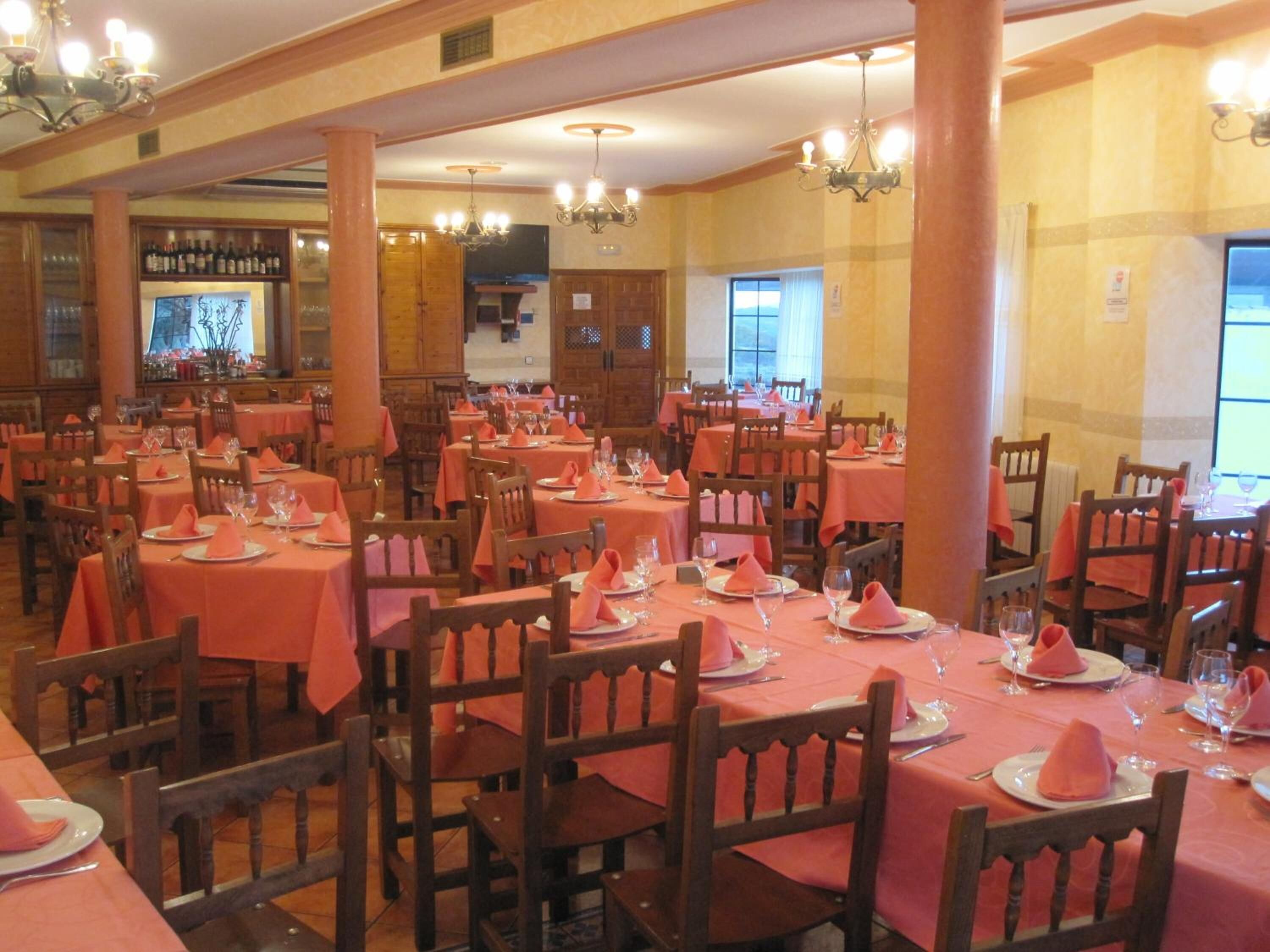 Restaurant amb diverses taules cobertes amb camases roses i cadires de fusta.