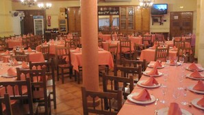 Un restaurante con varias mesas dispuestas, cubiertas con manteles y servilletas rosas, sillas de madera y un televisor montado en la pared.