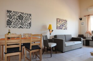A living room with a dining table, chairs, a sofa, and two wall-mounted lamps. - Rossa 18 (Oropos)