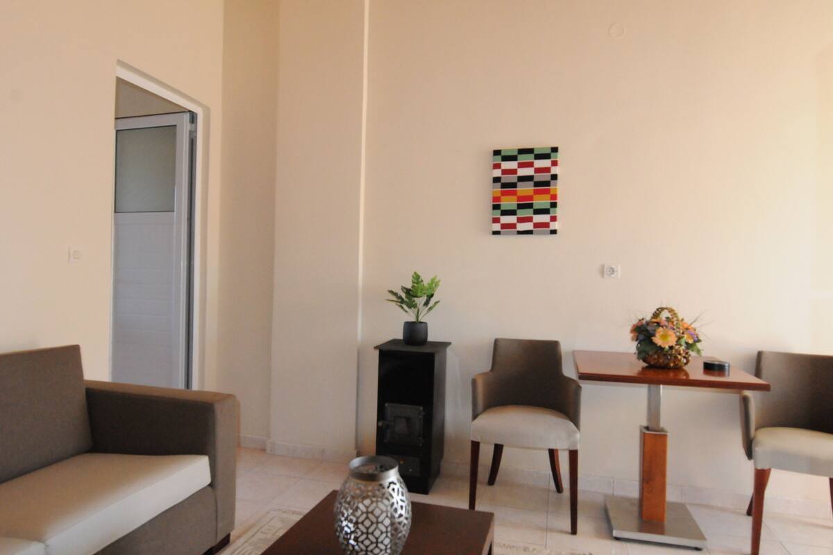 Uma sala de estar moderna com um sofá, duas poltronas, uma mesinha com um vaso e um objeto decorativo na parede.