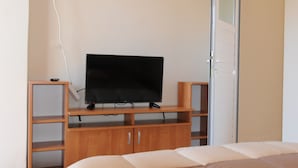 Une chambre à coucher avec un lit, un téléviseur posé sur un meuble en bois et une porte.
