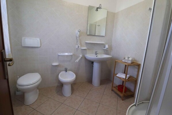 A bathroom with a toilet, bidet, sink, and a shelf with toiletries.