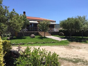 A two-story house with a red-tiled roof, a stone wall, and a front porch.