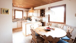 A kitchen with wooden cabinets, a central island, and a dining area with a round table and chairs. - Haus Fink (Innsbruck)