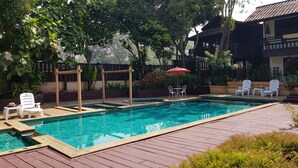 Piscina rectangular con un deck de madera alrededor, sillas de lounge blancas y una sombrilla roja.