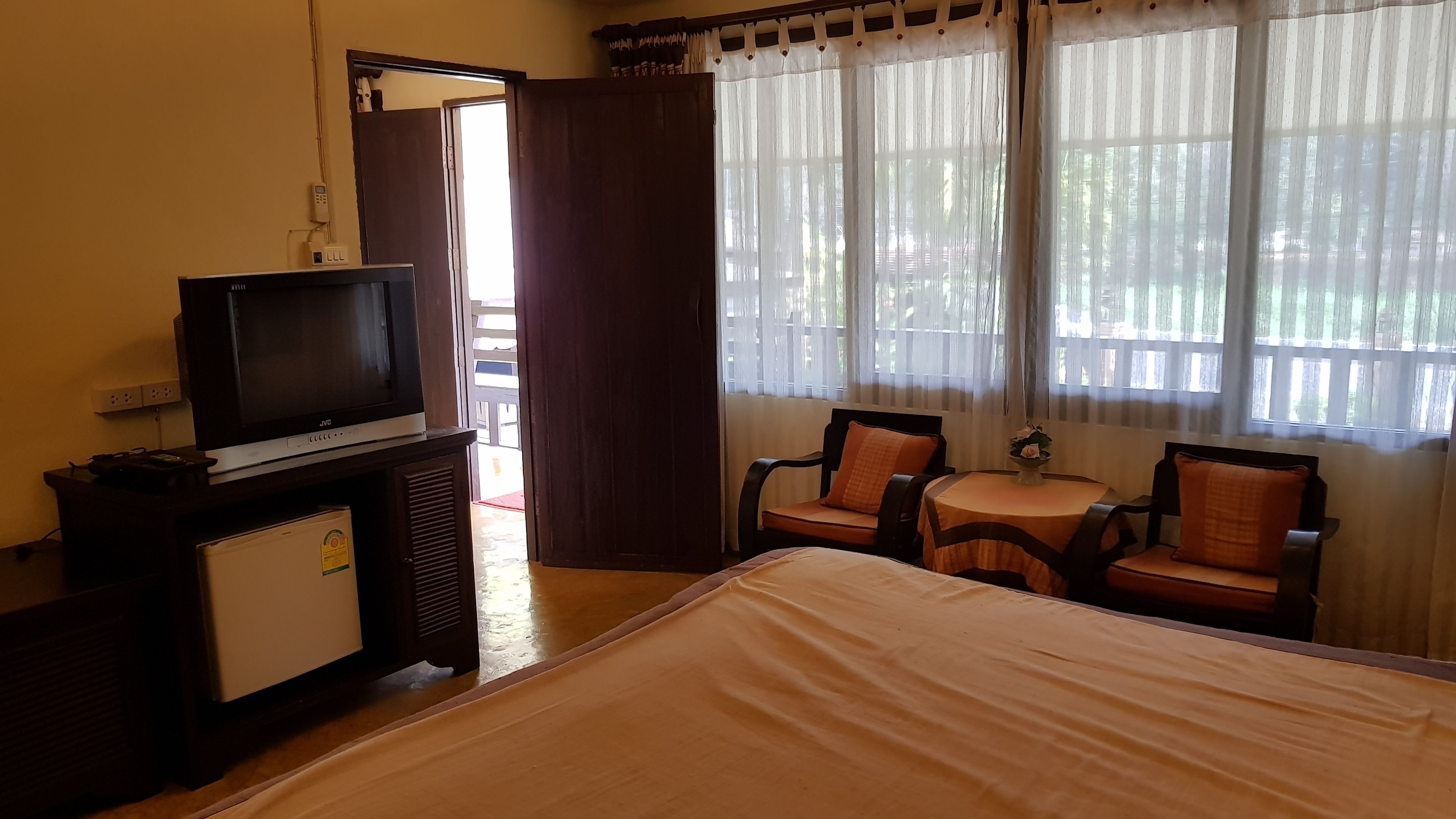A hotel room with a bed, a TV on a wooden cabinet, a small table with chairs, and a window with curtains.