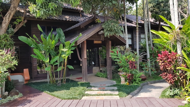 Un edificio de madera tradicional con recepción, rodeado de abundante follaje y un jardín cuidado.