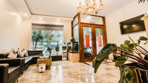 Un moderno vestíbulo de hotel con piso de mármol, un sofá de cuero negro, una mesa de centro de madera, una planta grande y un candelabro.