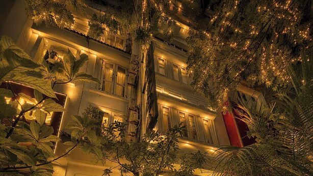 Entrada de un hotel con un cartel que dice 'ROYAL HOTEL', rodeada de abundante vegetación e iluminada con una luz cálida.