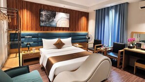 Habitación de hotel con una cama, dos sillones, un escritorio, una lámpara y un cuadro en la pared.