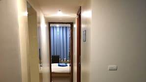 Un pasillo de hotel con un estampado de cuadros en el suelo, una cama con colcha azul y una puerta que da a una habitación.