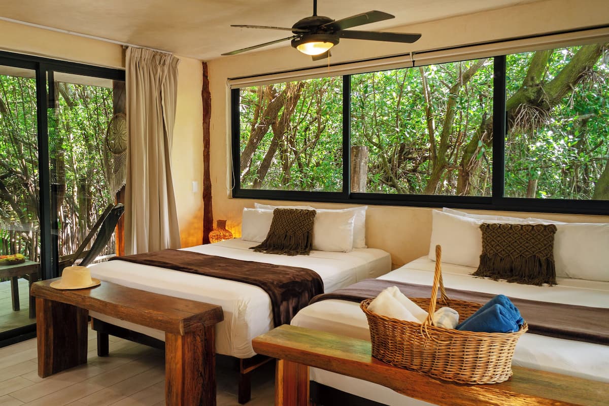 A bedroom with a large window, a ceiling fan, a bed with white linens, a wooden bench, and a wicker basket.