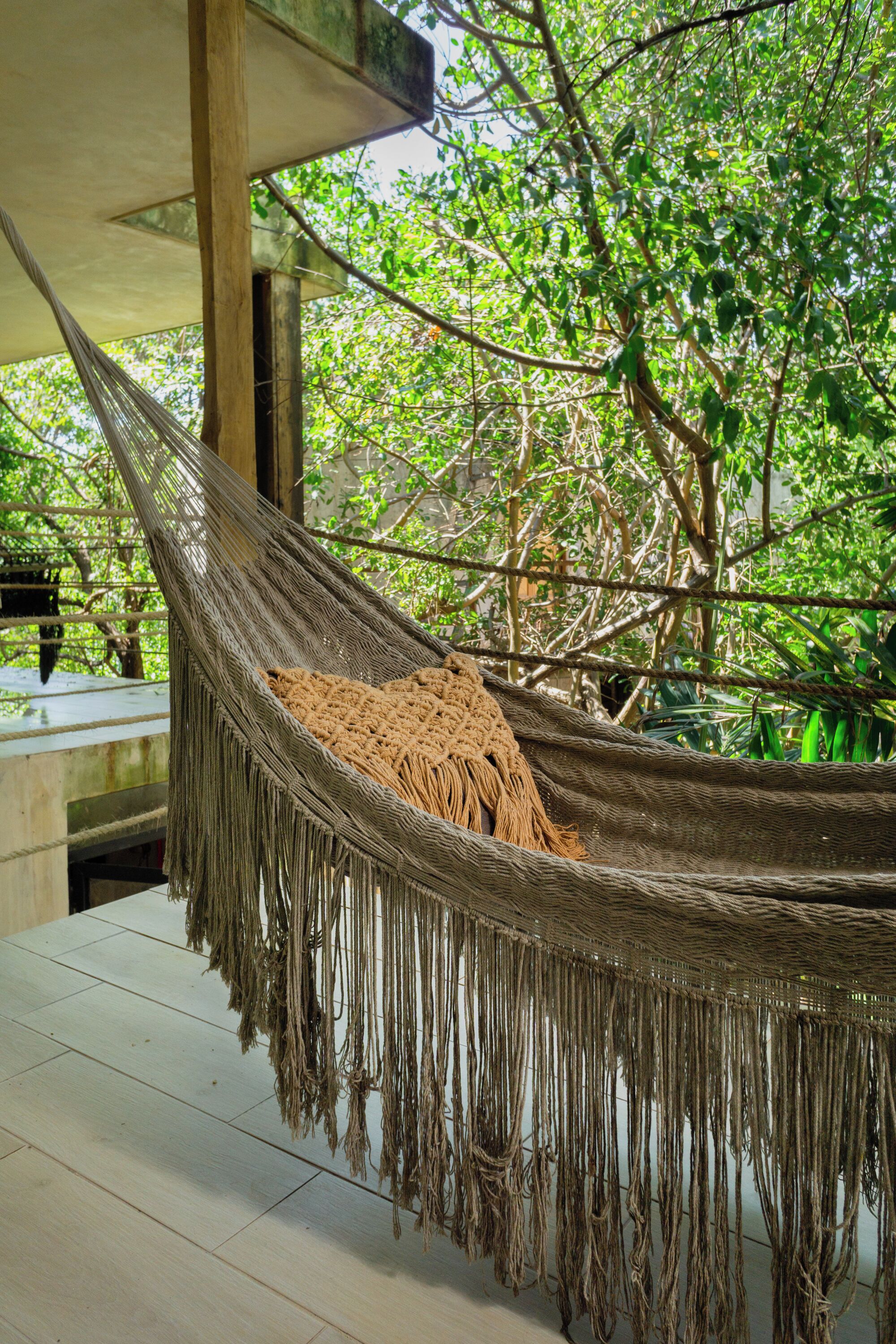 A hammock suspended between wooden beams, with a view of lush green trees and a tiled floor.