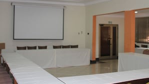 A conference room with a long table, chairs, a projector screen, and a door with an exit sign. - Ruby Kay Hotel (Accra)