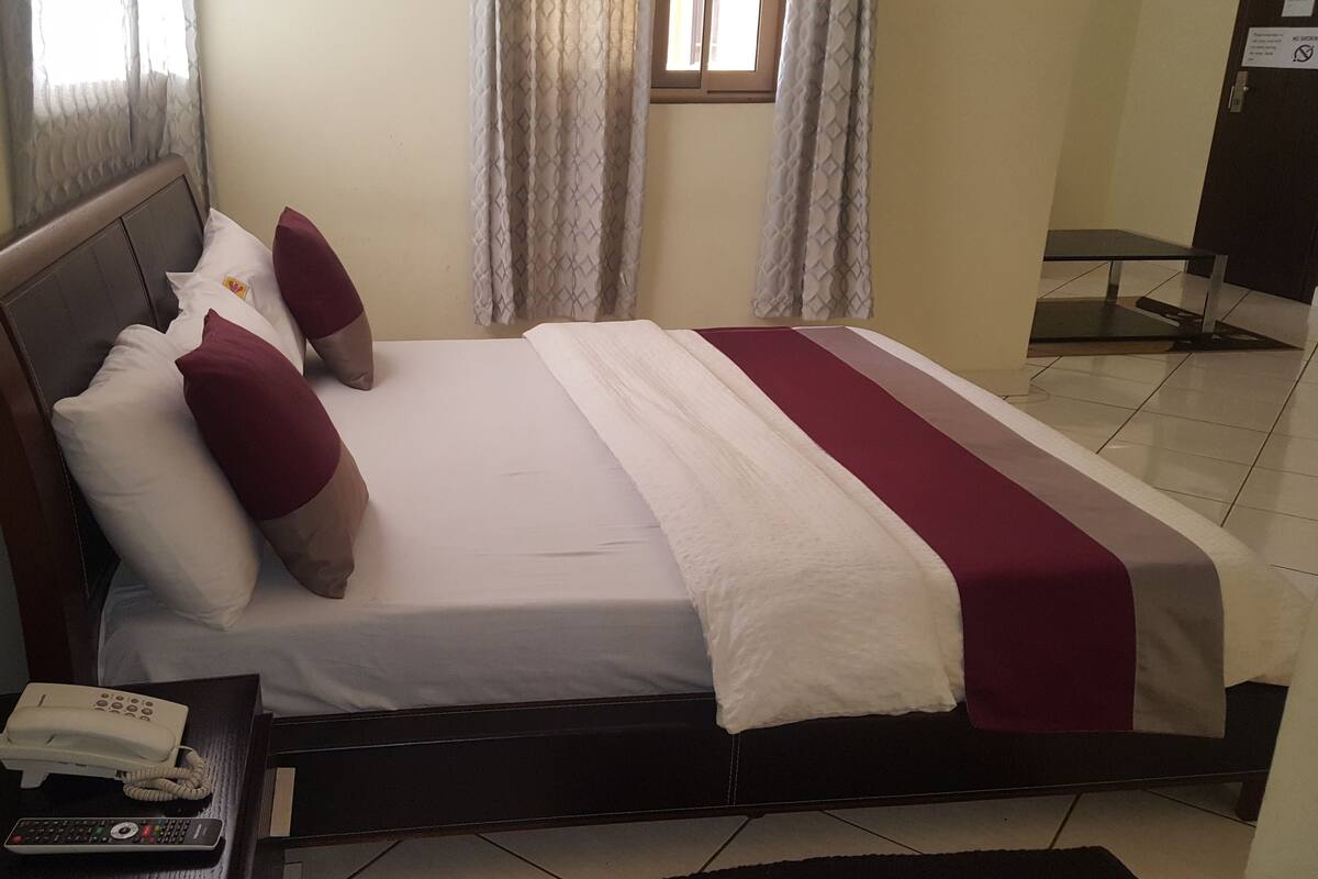 Habitación de hotel con cama, mesita de noche con teléfono y control remoto, y ventana con cortinas.