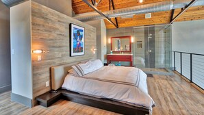 Un dormitorio moderno con techo de madera, una cama grande, cabina de ducha de vidrio y tocador rojo.