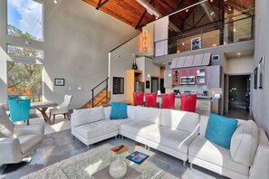 A modern living room with a sectional sofa, a coffee table, and a view of the kitchen area. - Romantic Hill Country Luxury - Perfect getaway for two! (Wimberley)