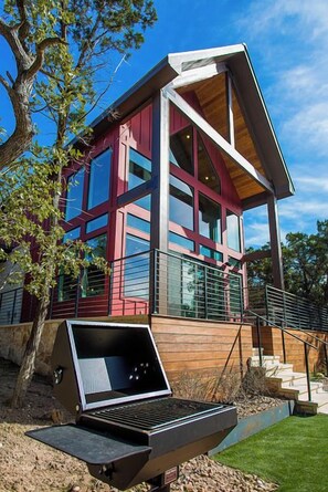 A modern house with a red and white exterior, large windows, and a wooden deck. - Romantic Hill Country Luxury - Perfect getaway for two! (Wimberley)