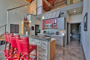A modern kitchen with a central island, red bar stools, and a staircase leading to an upper level. - Romantic Hill Country Luxury - Perfect getaway for two! (Wimberley)