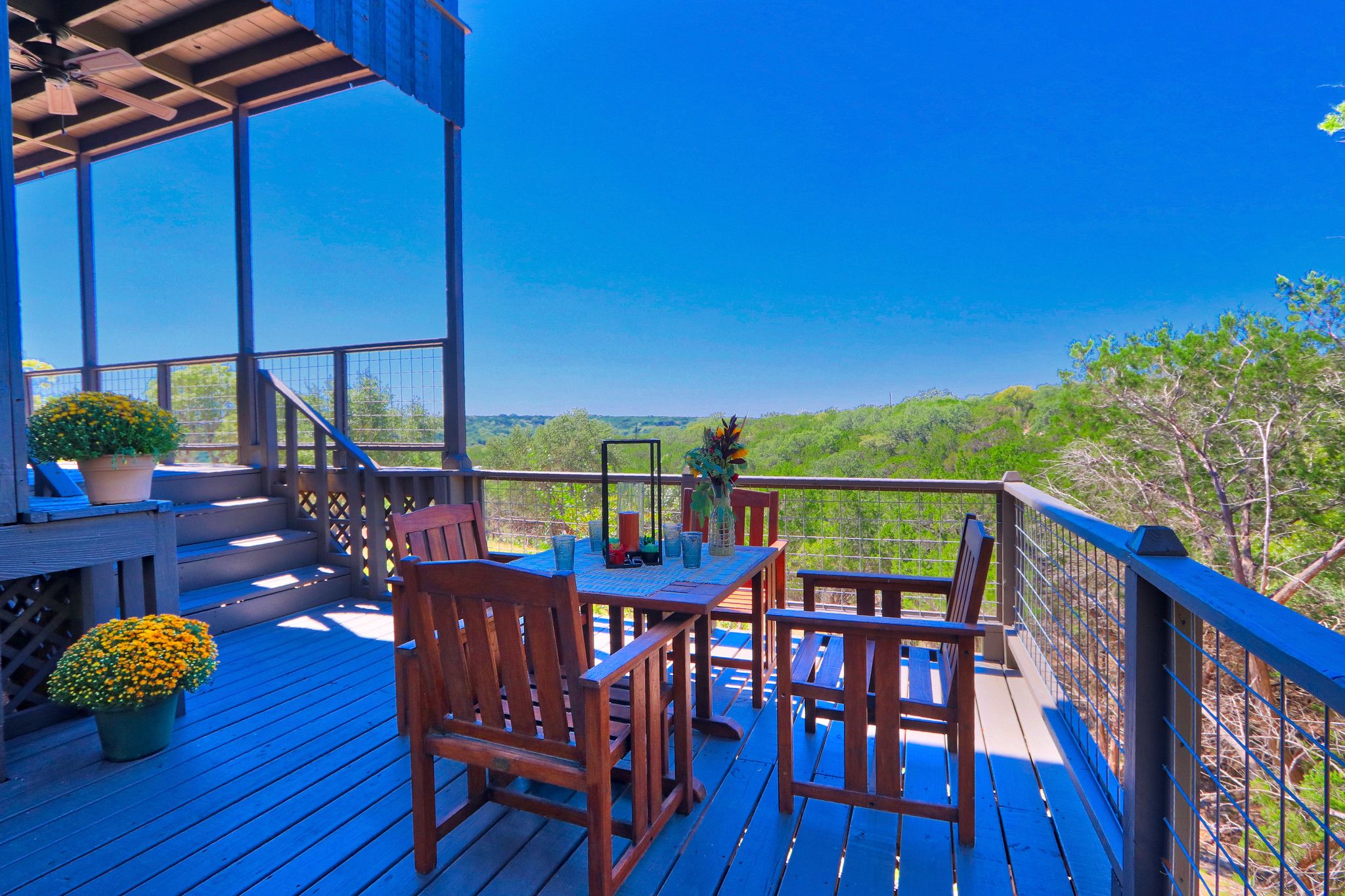 A wooden deck with outdoor furniture and a railing overlooking a forested area.