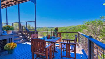 A wooden deck with outdoor furniture and a railing overlooking a forested area.