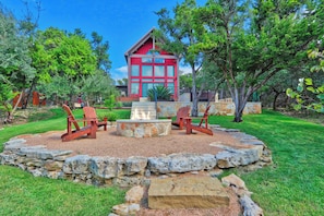 A red wooden cabin with a stone fire pit and two wooden chairs in a landscaped garden. - Romantic Hill Country Luxury - Perfect getaway for two! (Wimberley)