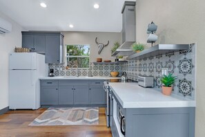 A modern kitchen with grey cabinets, a white refrigerator, patterned backsplash, and a central island with a sink and a toaster. - Wimberley Hill Country Retreat | Sleeps 31, Firepits, Cabins & Scenic Views (Wimberley)