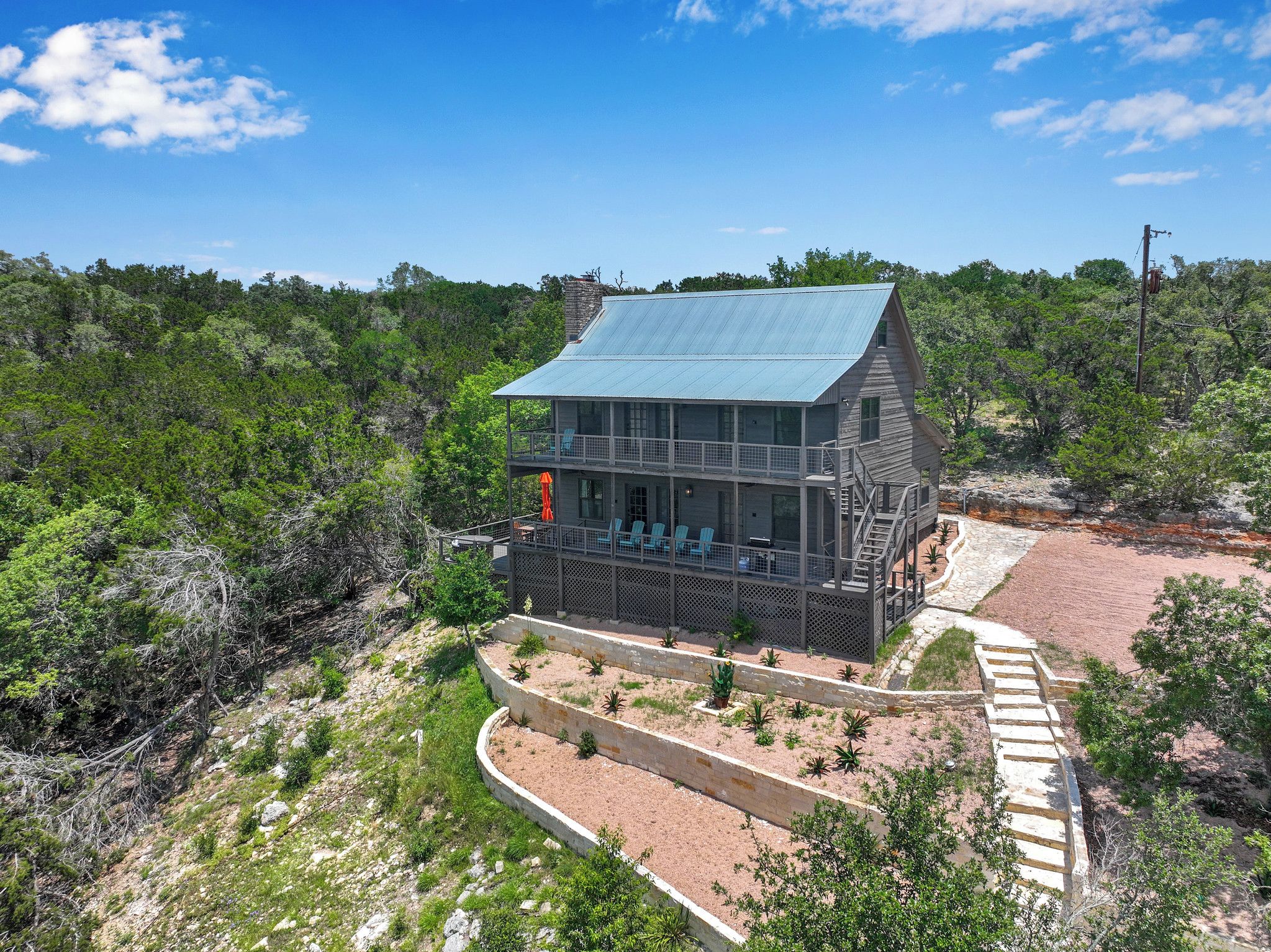 A two-story building with a balcony, surrounded by a landscaped garden and dense forest.