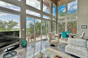 A spacious living area with a large TV, comfortable seating, and a balcony with a view of the landscape. - Romantic Hill Country Luxury - Perfect getaway for two! (Wimberley)