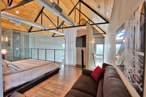 A modern bedroom with a bed, a sofa, a TV, and a large window. - Romantic Hill Country Luxury - Perfect getaway for two! (Wimberley)