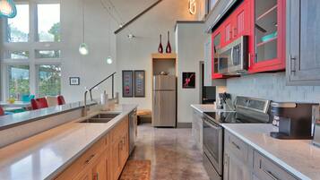 A modern kitchen with a large island, stainless steel appliances, and red cabinetry.