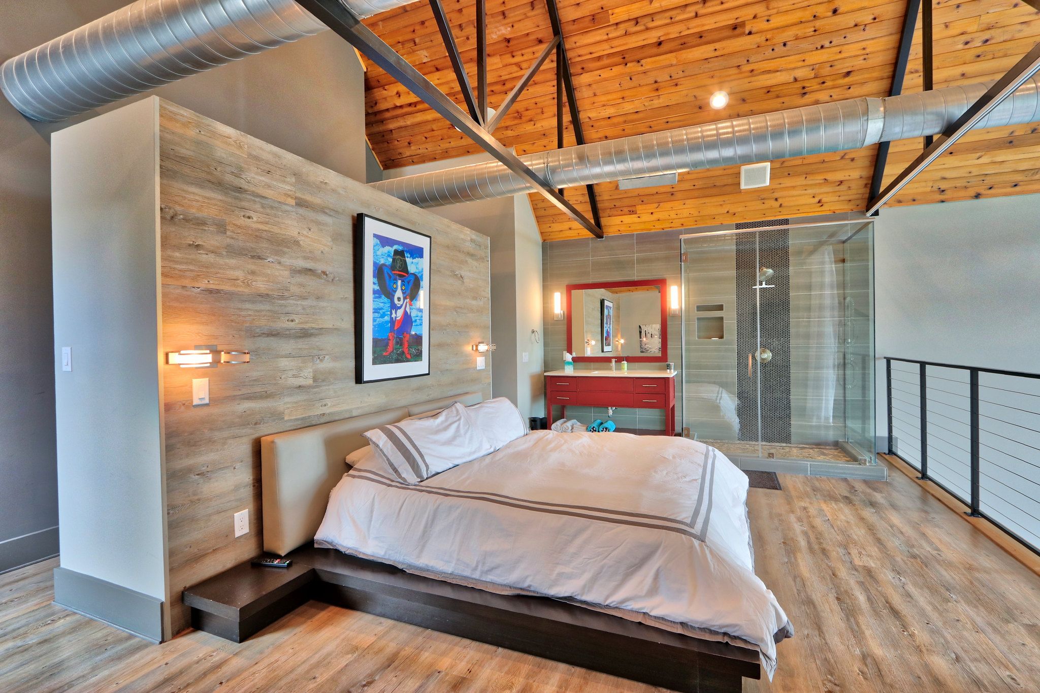 A modern bedroom with a wooden ceiling, a large bed, a glass shower, and a red vanity.