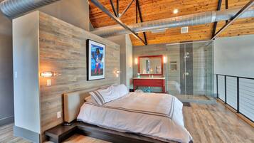 A modern bedroom with a wooden ceiling, a large bed, a glass shower, and a red vanity.