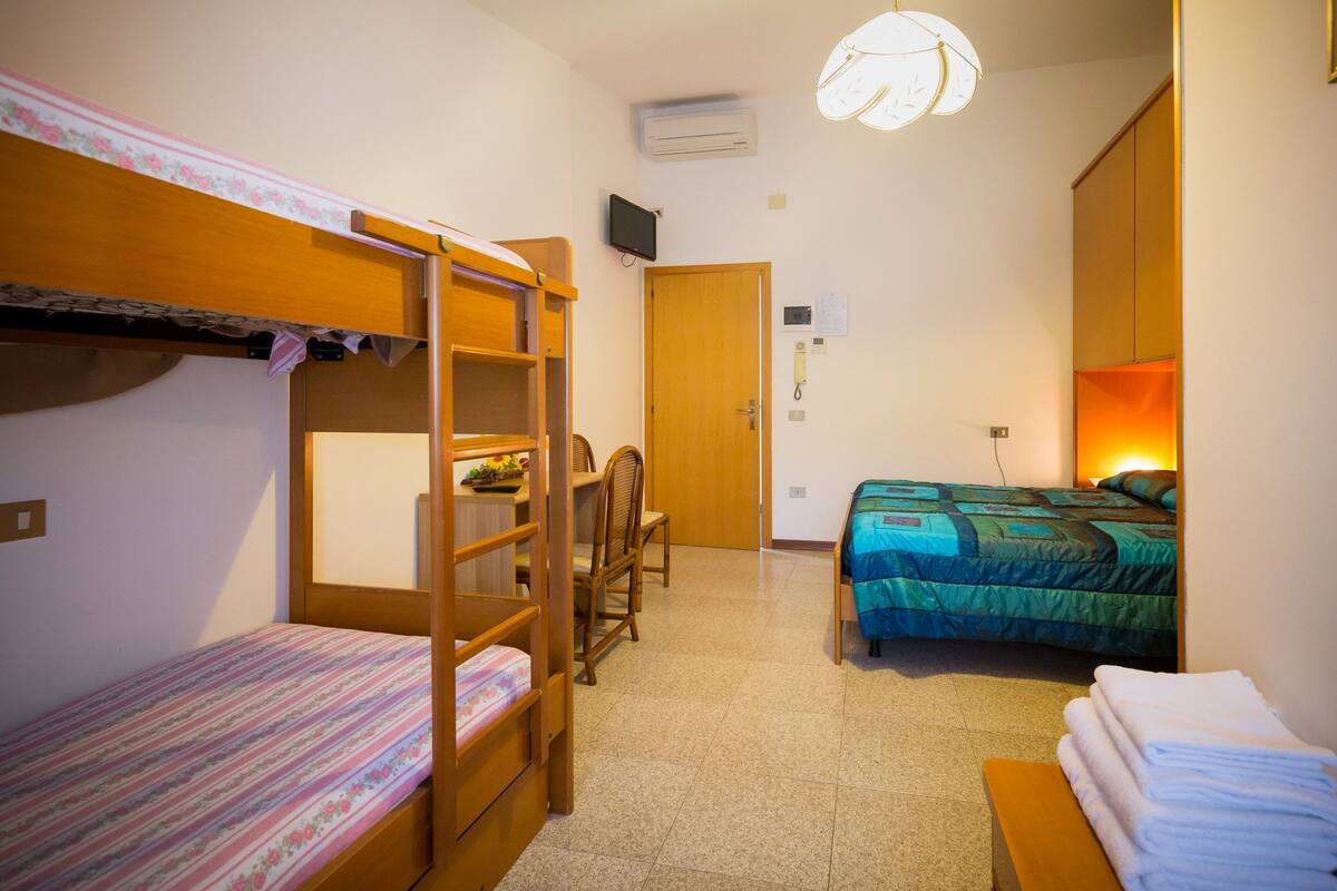 A dormitory room with bunk beds, a desk, and a chair.