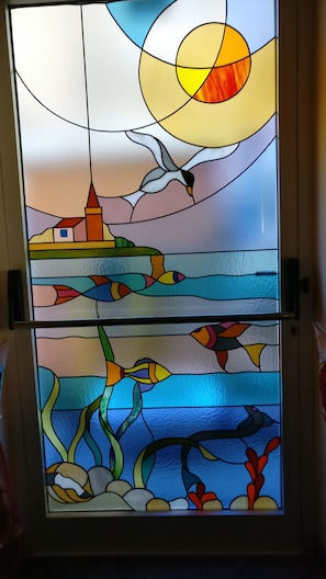 A stained glass window with a landscape scene, including a lighthouse, birds, and fish. - Hotel Fabrizio (Caorle)