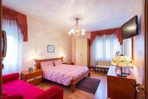 A well-lit bedroom with a bed, bedside tables, a desk, and a television. - Hotel Fabrizio (Caorle)