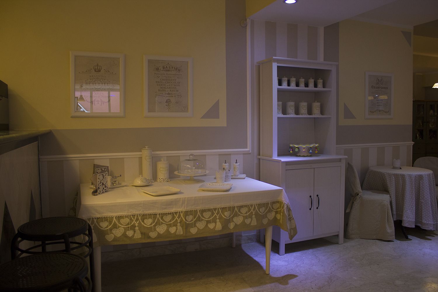 A dining area with a table set for two, a white cabinet with shelves, and framed certificates on the wall.