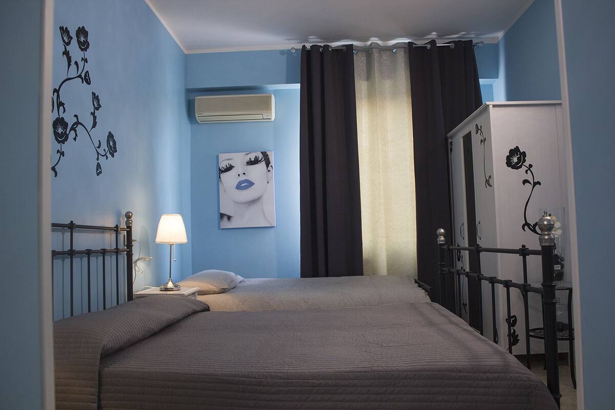 Quarto com cama, luminária de cabeceira, ar-condicionado na parede e janela com cortinas.