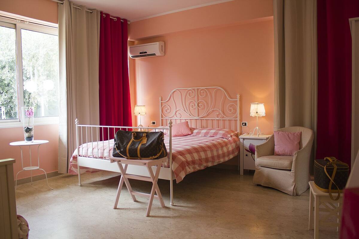 Quarto com cama, mesas de cabeceira, uma cadeira, uma mesinha e um ar condicionado.