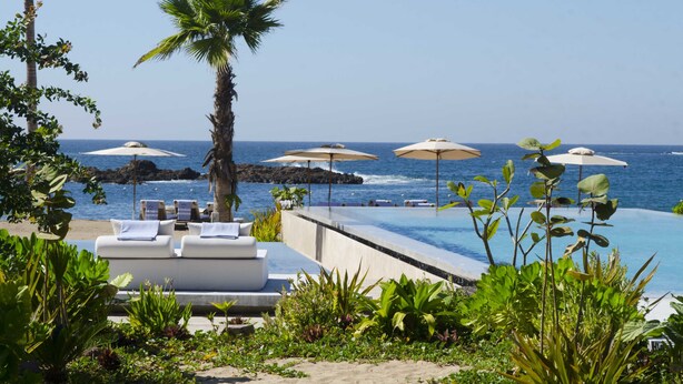 A poolside area with lounge chairs and umbrellas, overlooking the ocean.