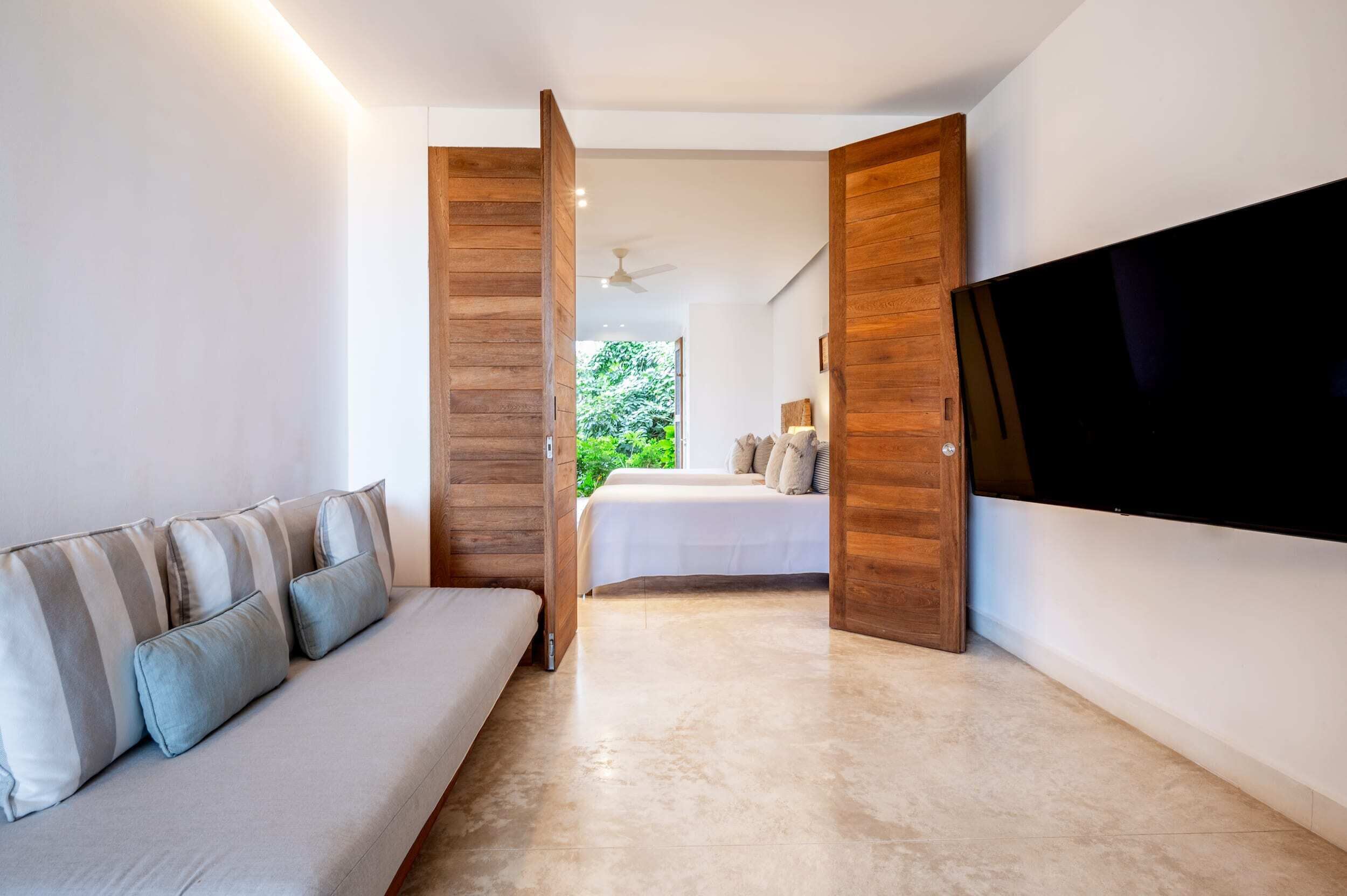 A modern hotel room with a sofa, a bed, a flat-screen TV, and wooden paneling.