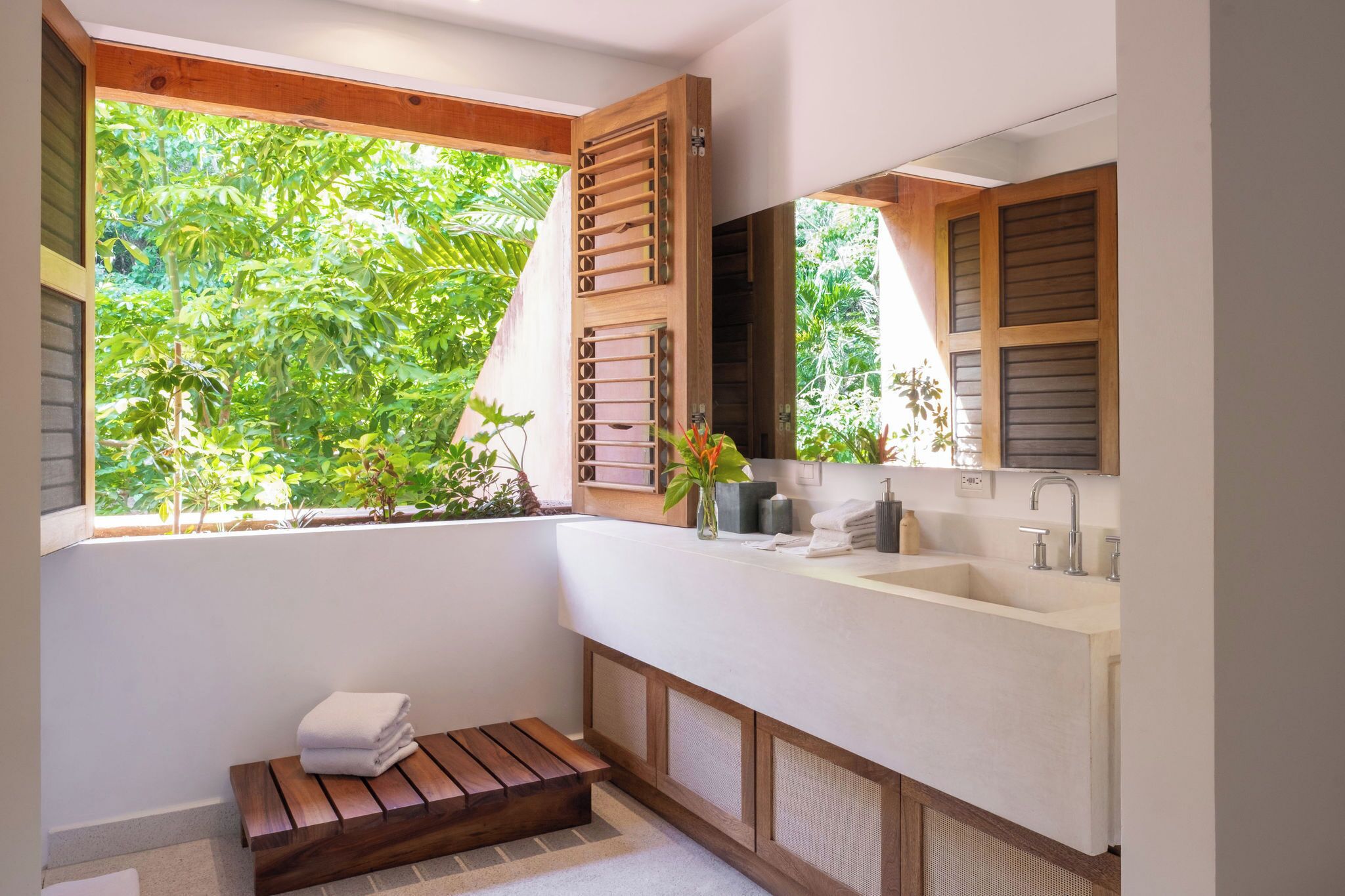 Un baño con un ventanal grande, contraventanas de madera, un lavamanos y una banca.