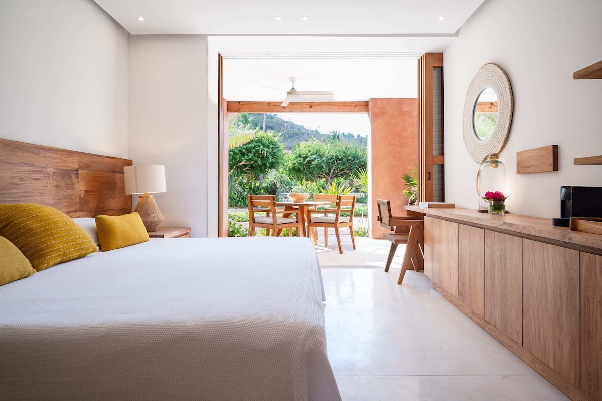 Un dormitorio con una cama grande, cabecera de madera y vista a un jardín a través de una puerta abierta.