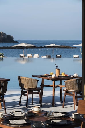 A dining area with a view of the sea, featuring tables, chairs, umbrellas, and a pool. - El Careyes Club & Residences (Costa Careyes)