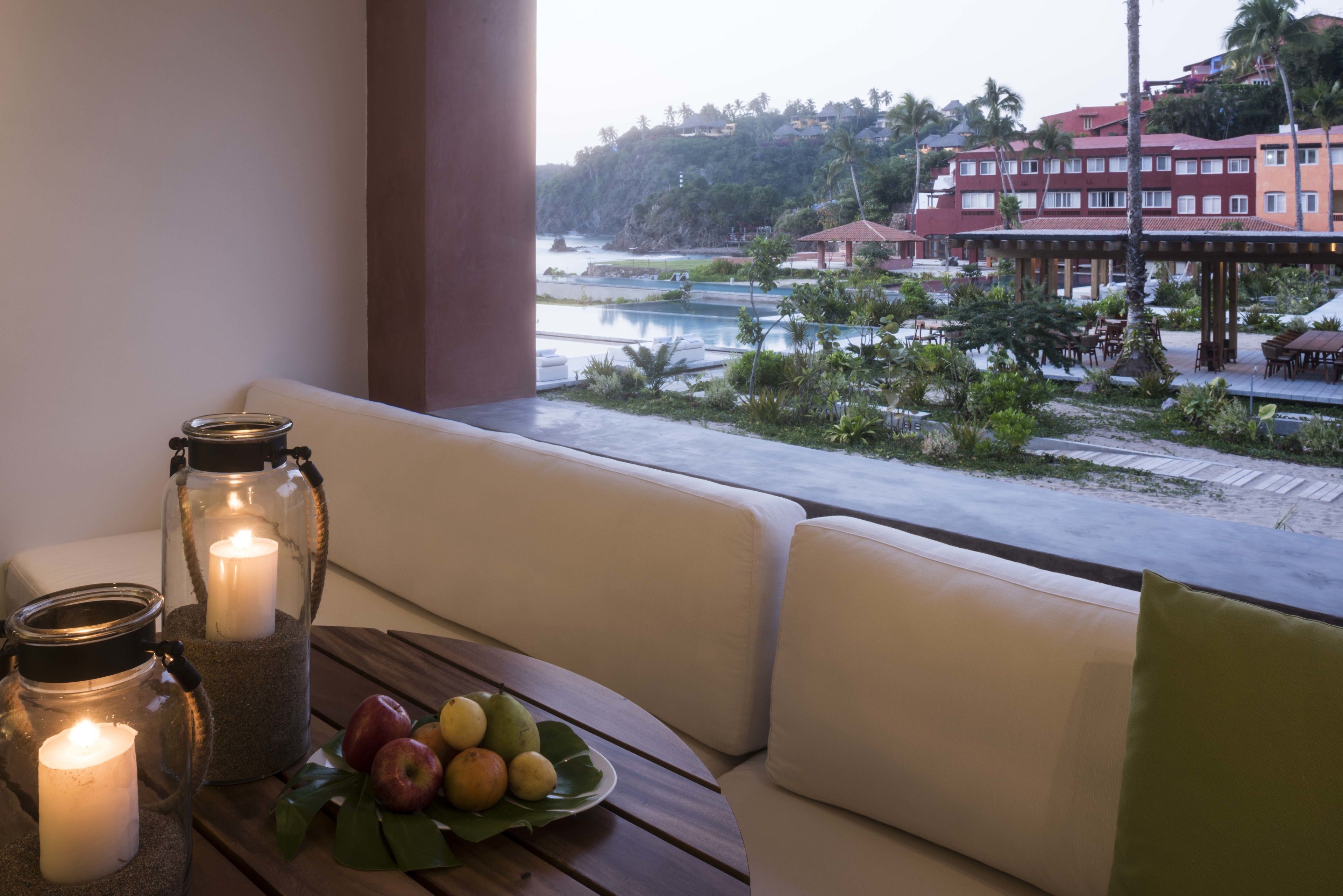 Un balcon donnant sur une piscine et des immeubles, une table avec des fruits et des bougies, et un canapé avec des coussins.