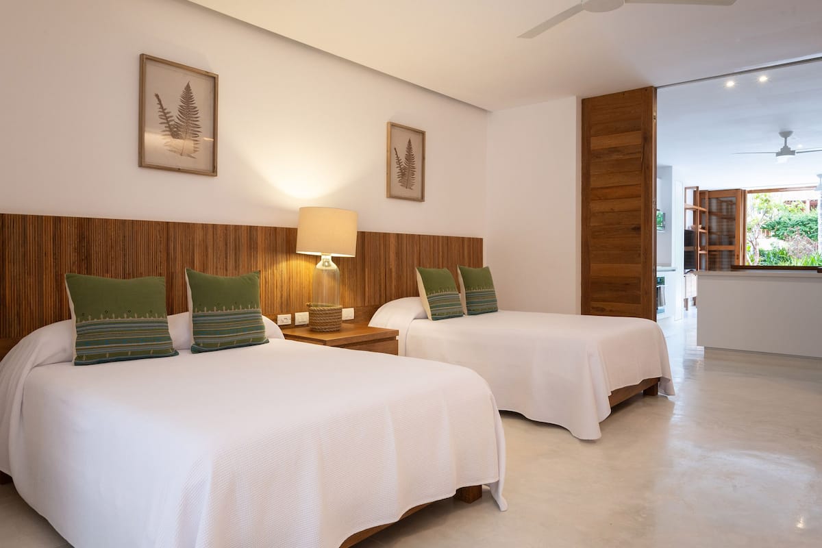 Habitación de hotel con dos camas, cabeceros de madera y arte decorativo con helechos en las paredes.