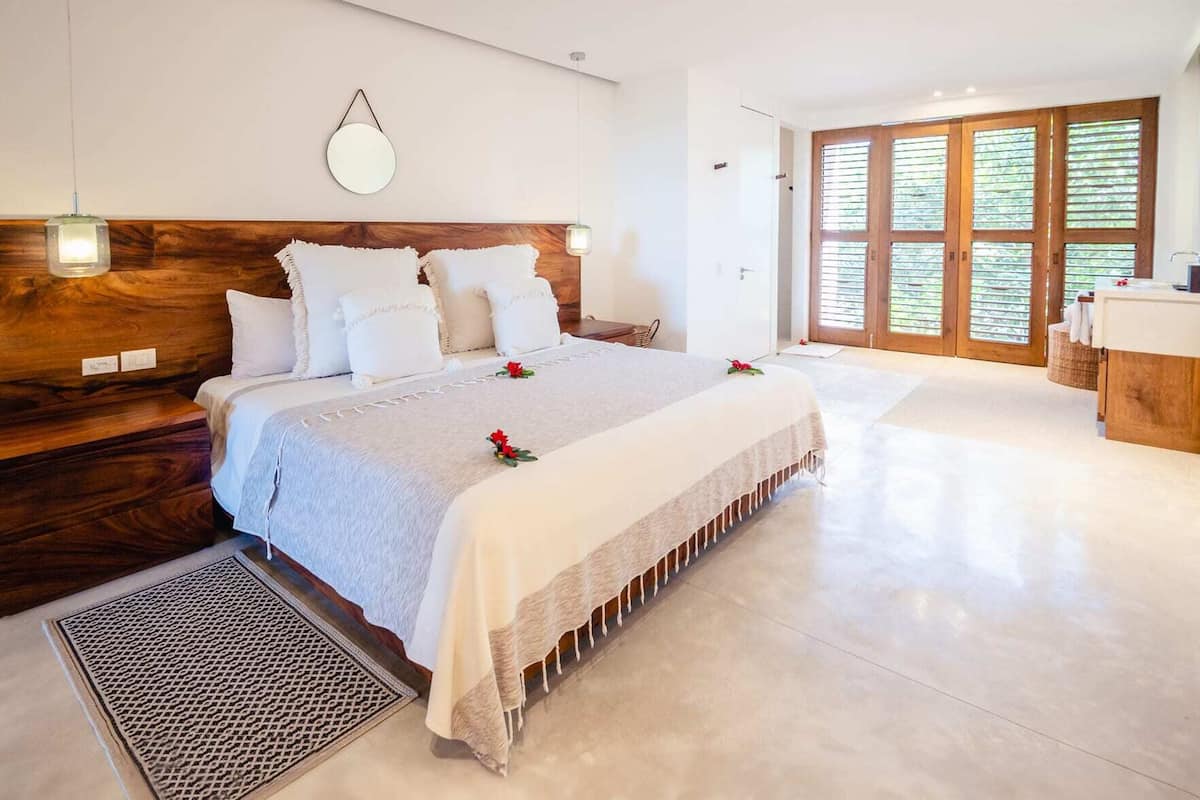 Un dormitorio amplio con una cama grande, cabecera de madera y vistas a una puerta y persianas de madera.