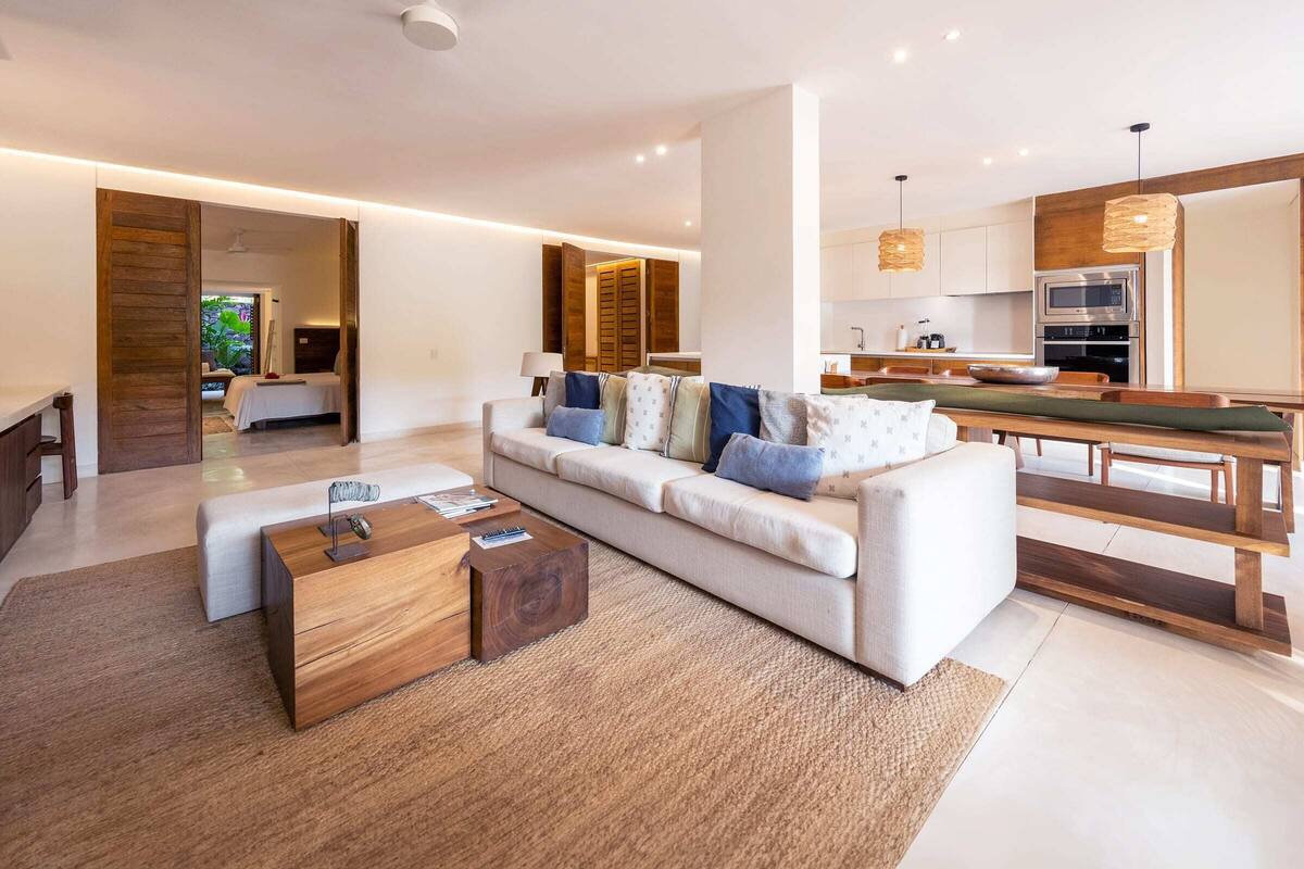 Una sala de estar moderna con sofá, mesa de centro y comedor con muebles de madera.