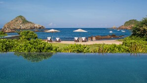 An infinity pool with a view of the sea, beach chairs, and umbrellas.
