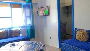 Una habitación con una cama de diseño azul y blanco, una mesita con un cubre decorativo, un televisor montado en la pared y un espejo.